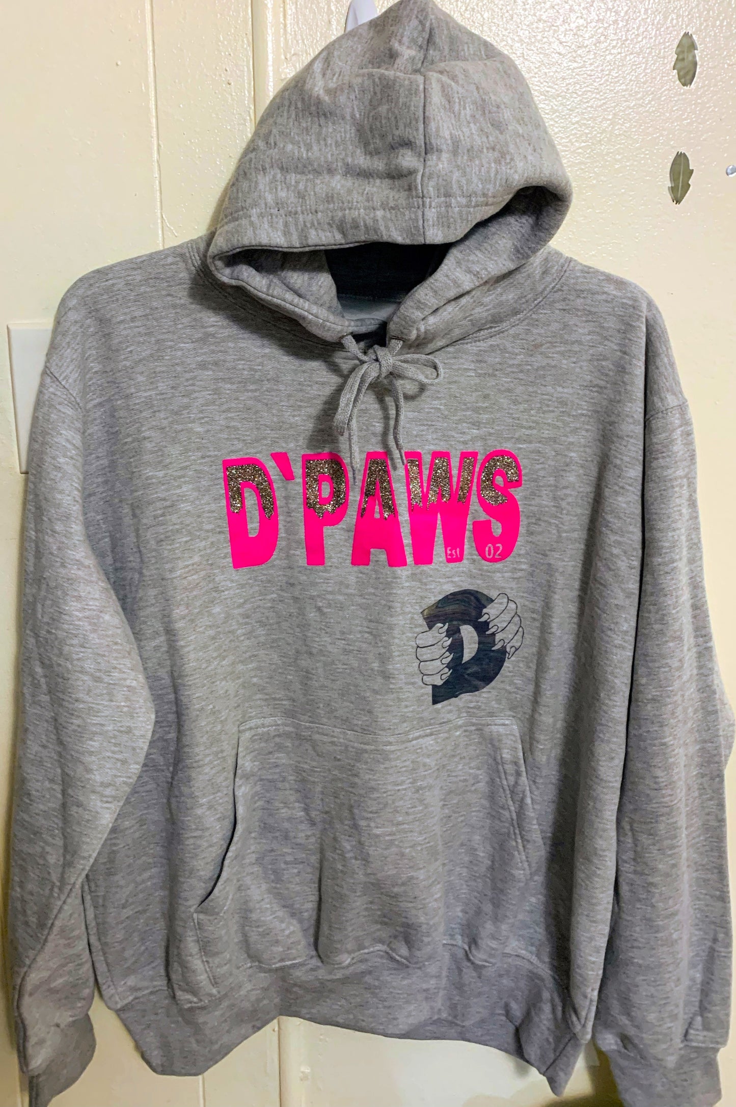 Adult sized, gray, long-sleeved hoodie.  Has brand name in hot pink and silver and black block, heat press vinyl.  Black glitter vinyl logo mid-left front.  Has draw string closure at hood.